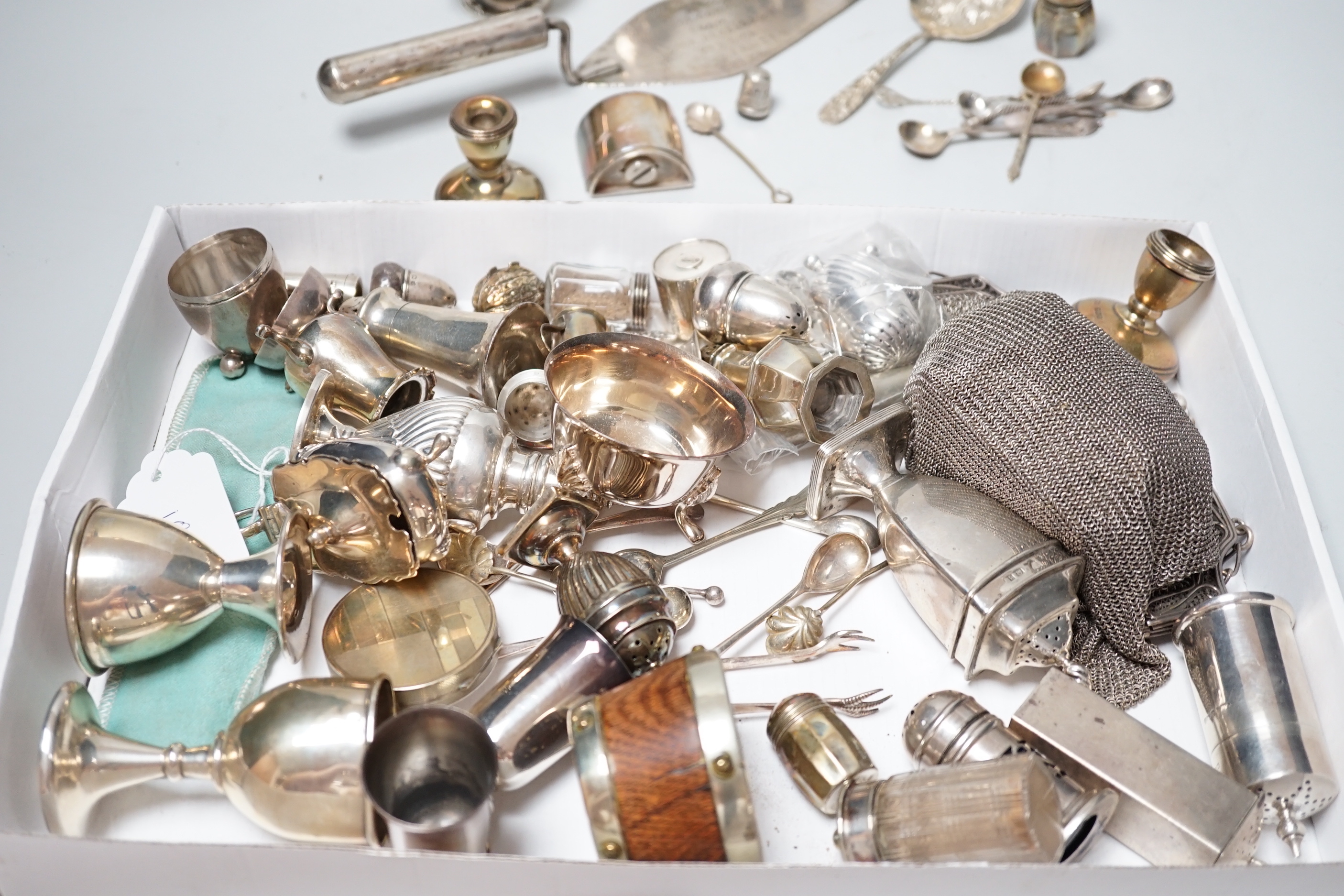 A collection of assorted small silver including condiments, spoons, egg cup, pill box, comb, Tiffany & Co pen, dwarf candlesticks, and other items including a plated evening bag and African trowel.